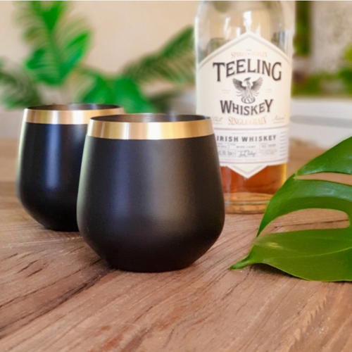 black drinkware with brass rim next to a bottle of drink