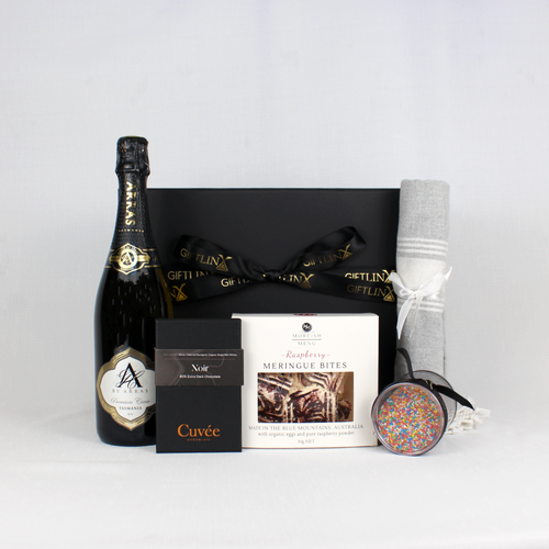 black gift box standing behind a dark bottle of Australian sparkling wine, chocolate, meringue and a turkish towel