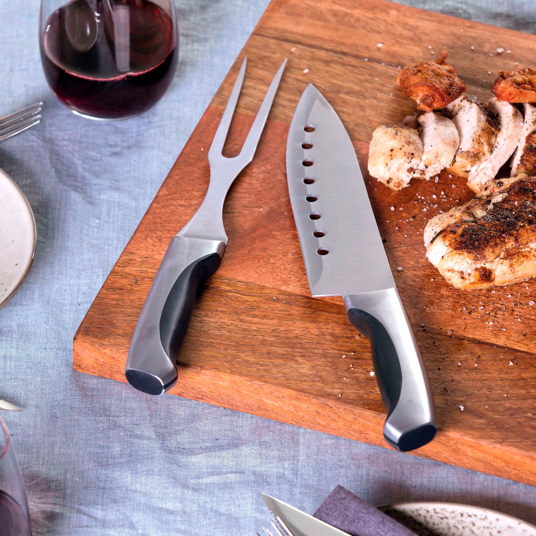lifestyle photograph with a carving board and sliced meat next to the stainless steel carving set and a glass of red wine