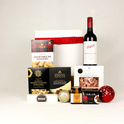 white gift box with red ribbon standing behind a bottle of Australian red wine, shortbread, honey coated popcorn, chocolate coated almonds, nougat, raspberry meringue and a Christmas pudding with a bottle of sauce