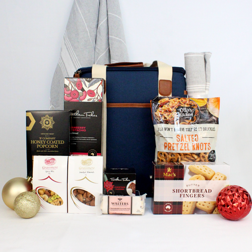 luxury insulated canvas bcooler bag surrounded by picnic products such as pretzels, shortbread biscuits, cranberry and pistachio crackers, honey coated popcorn, smoked almonds, spicy mix, nougat bar and a small christmas pudding