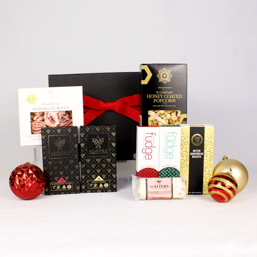 small black gift box with red ribbon standing behind sweet Christmas treats including fudge, chocolate, meringue bites, nougat and honey coated popcorn