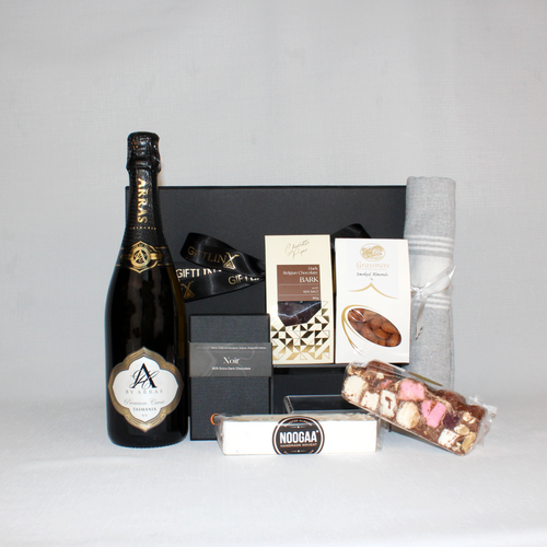 black gift box behind a bottle of Australian sparkling wine in a black and gold bottle next to chocolate, rocky road, nougat, smoked almonds and a Turkish hand towel