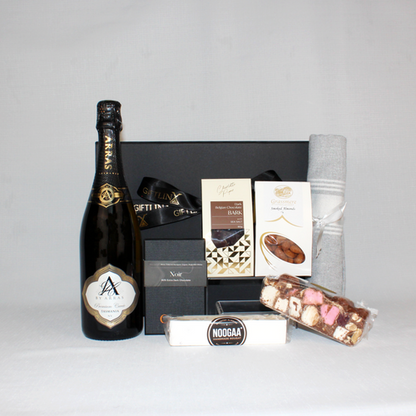 black gift box behind a bottle of Australian sparkling wine in a black and gold bottle next to chocolate, rocky road, nougat, smoked almonds and a Turkish hand towel