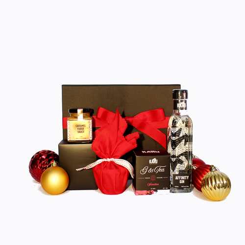 black gift box with red ribbon behind a bottle of Australian Gin with a box of G&T teabags and a Christmas pudding with sauce surrounded by Christmas baubles