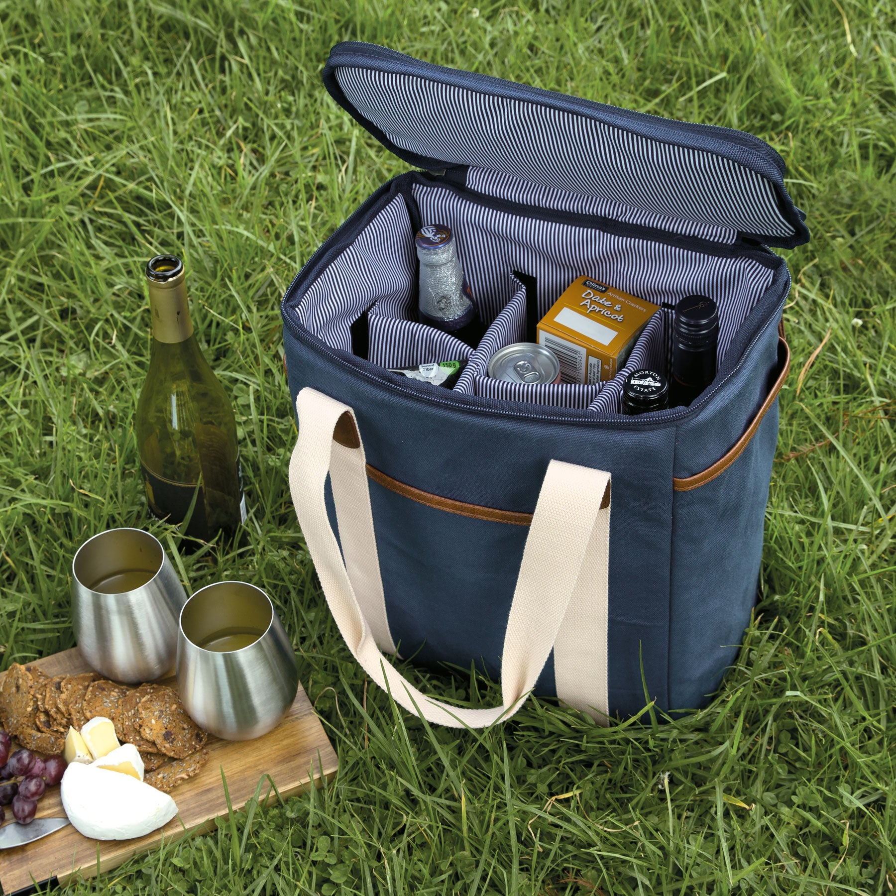 Lifestyle image of navy blue wine cooler on grass filled with picnic foods and wine next to a cheese board