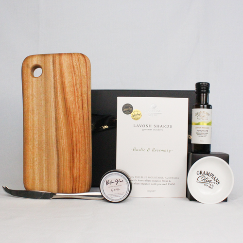 Black magentic gift box with ribbon filled with handmade timber cheese board and single stainless steel cheese knife, Australian made lavosh shards, infused olive oil with dipping bowl and luxury soy candle tin.