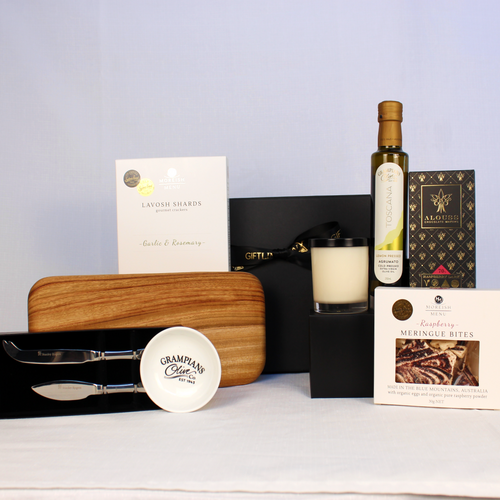 Black magnetic gift box with complimentary ribbon includes a  handmade timber cheese board, cheese knife set, Infused olive oil with dipping bowl, lavosh shards meringue bites, handmade chocolate and a luxury soy candle jar.