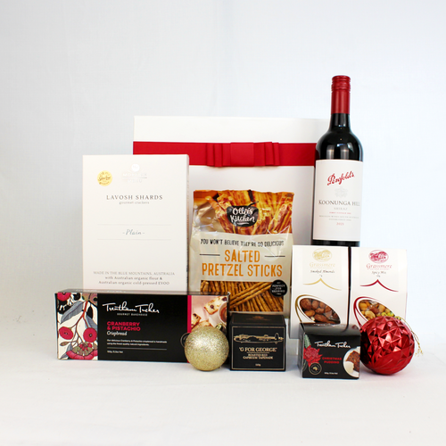 a white gift box with red ribbon standing behind a bottle of Australian red wine and savoury snacks including pretzels, lavosh shards, crispbread, smoked almonds, roasted capsicum tapenade and a Christmas pudding