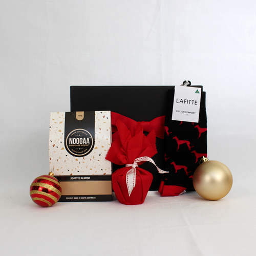 black gift box behind a box of nougat pieces next to a Christmas pudding in red fabric and a pair of cotton corporate socks surrounded by Christmas baubles
