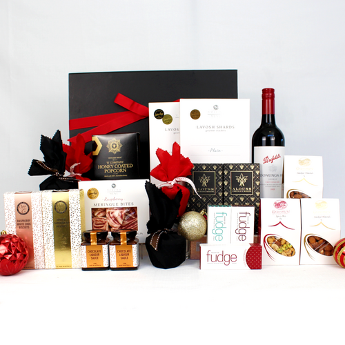 a balck gift box with red ribbon standing behind a range of Australian products including wine, chocolate, christmas pudding and sauce plus some savoury snacks of roasted almonds and lavosh shards