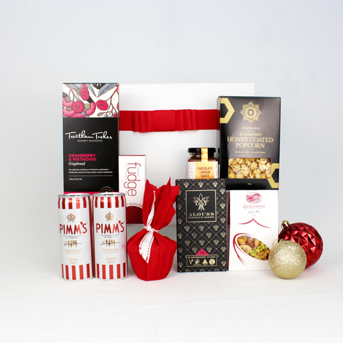 white gift box with red ribbon standing behind 2 cans of premixed Pimm's cocktails alongside a selection of sweet and savoury festive snacks