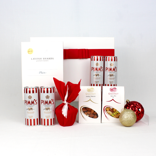 white gift box with red ribbon standing behind 4 cans of red and white striped premixed Pimm's lemonade, lavosh shards, smoked almonds and spicy nut mix alongside a Christmas pudding in red fabric
