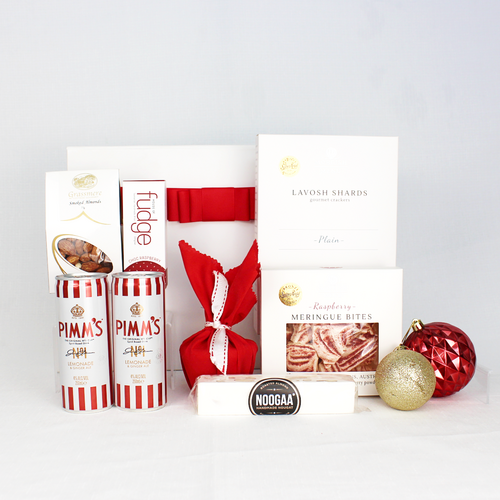 white gift box with red ribbon standing behind 2 cans of Pimm's premade cocktails with fudge, smoked almonds, nougat, meringue, lavosh shards and a Christmas pudding in red cloth