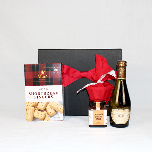 black gift box with red ribbon behind Australian made shortbread, Christmas pudding, pudding sauce and a piccolo of sparkling wine