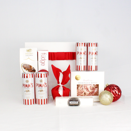 white gift box with red ribbon standing behind red and white products including 4 striped cans of Pimm's, fudge, smoked almonds, nougat bar, meringue bites and a Christmas pudding