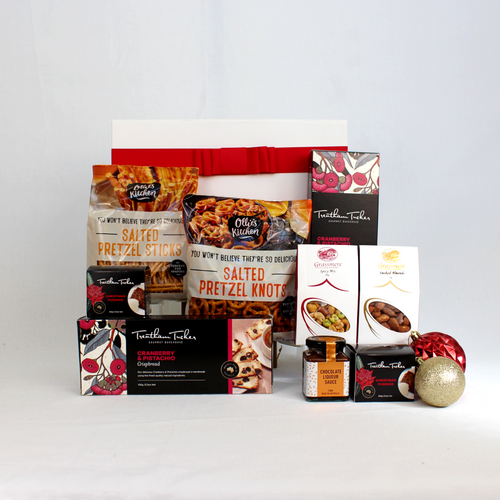 a white and red gift box standing behind a range of savoury Christmas snacks including pretzels, crispbread, smoked almonds, spicy nut mix and two Christmas puddings with sauce surrounded by Christmas baubles for decoration