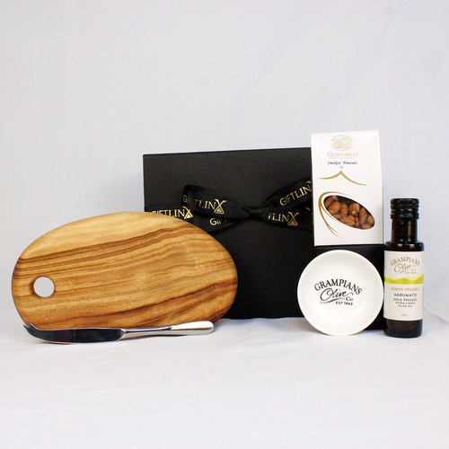 A black gift box with ribbon conatining a small handcrafted cheese board with a stainless steel cheese knife, smoked almonds, infused olive oil and a dipping bowl