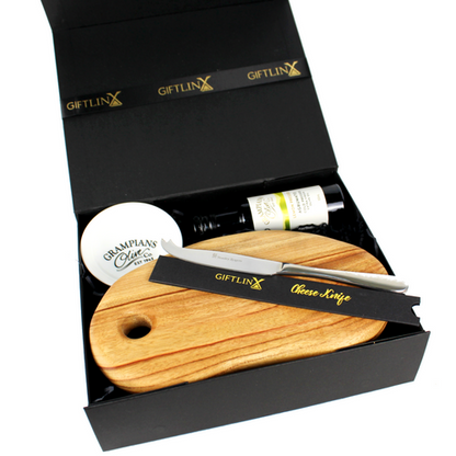 Handmade timber serving board with cheese knife laying on top. Packed in a black magnetic box with black crinkle paper fill alongside a small bottle of infused olive oil and dipping bowl