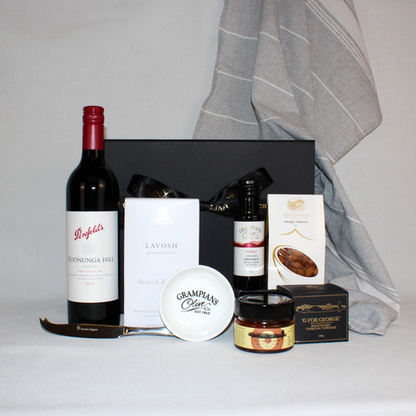 black gift box behind a penfolds red wine with lavosh, smoked almonds, tapenade a cheese knife and dipping bowl with a grey hand towel hanging in the background