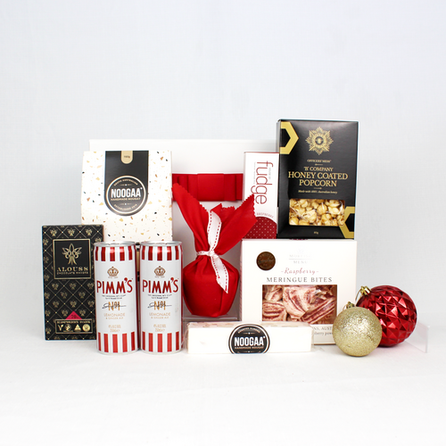 white gift box with red ribbon standing behind 2 cans of premixed Pimm's cocktails, a christmas pudding in red cloth, honey coated popcorn, raspberry meringue bites, a selection of nougat and Australian hand made chocolate