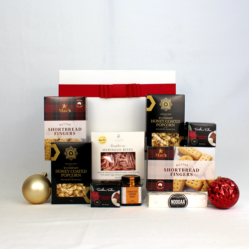 A white and red gift box behind a range of sweet festive treats including honey coated popcorn, butter shortbread, Christmas puddings and sauce, raspberry meringue and nougat surrounded by Christmas baubles.