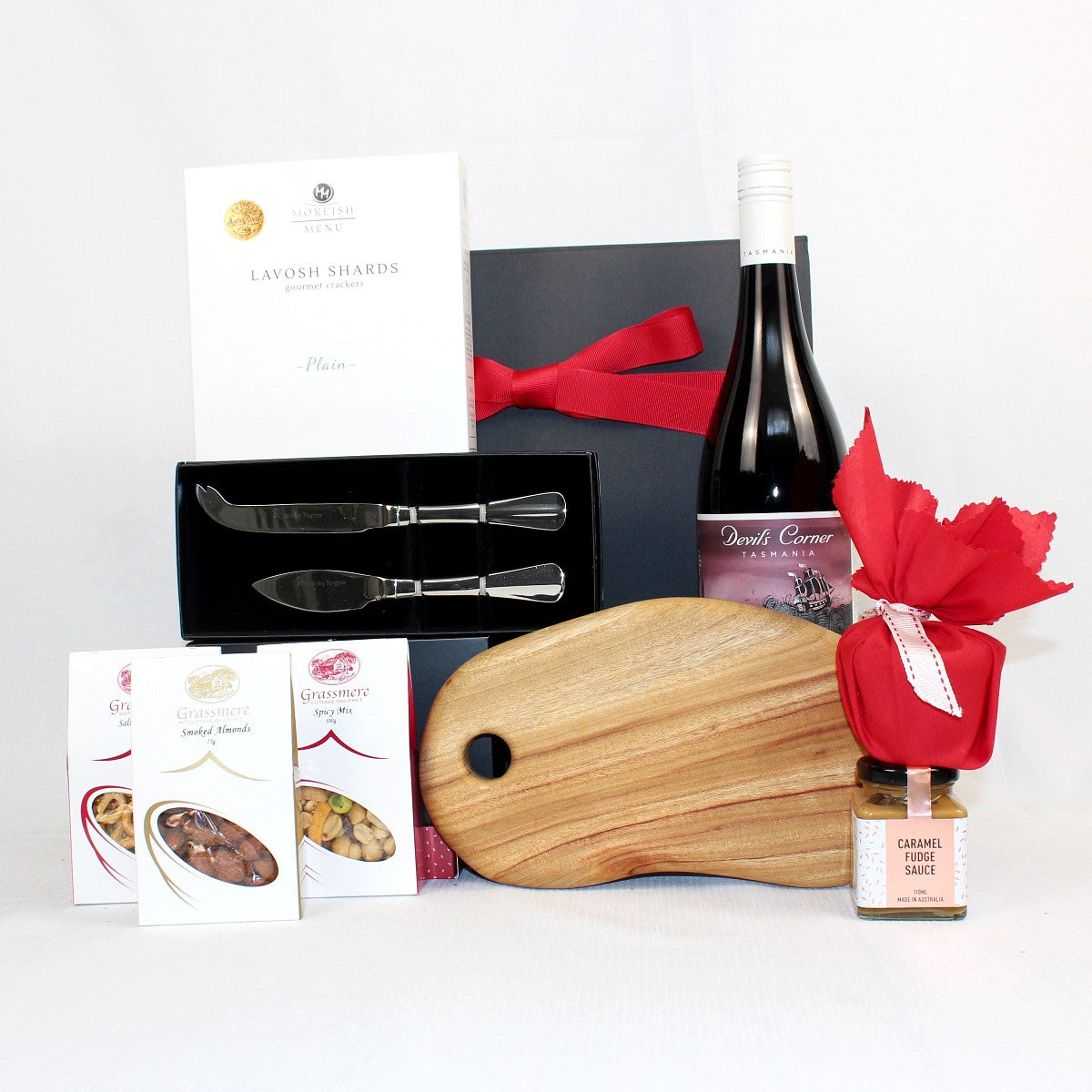 black gift box with festive red ribbon standing behind a handmade timber cheese board, cheese knife set, Australian made lavosh shards, pretzels, smoked alminds, spicy mix Christmas pudding in red fabric and pudding sauce with Australian wine