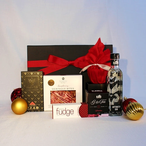black gift box with red ribbon standing behind a bottle of Australian Gin with gin teabags to infused the gin, Christmas pudding, fudge, chocolate and meringue bites with Christmas baubles