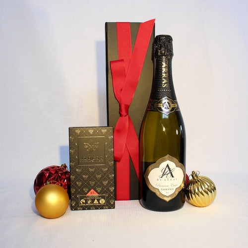 black gift box with red ribbon behind a bottle of Australian sparkling wine and handmade chocolate surrounded by Christmas baubles