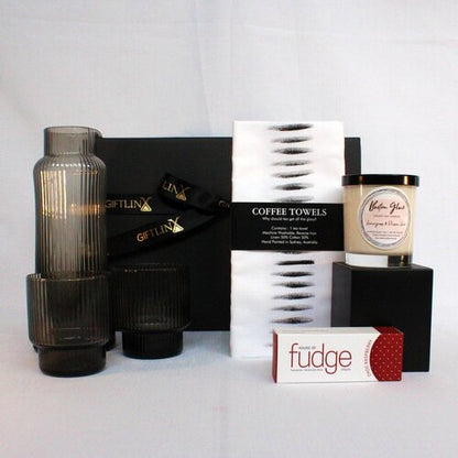 A beautiful homewares gift hamper with ribbed, handblown glass carafe and matching glassware, luxury soy candle jar, Australian made fudge and a linen blend kitchen towel