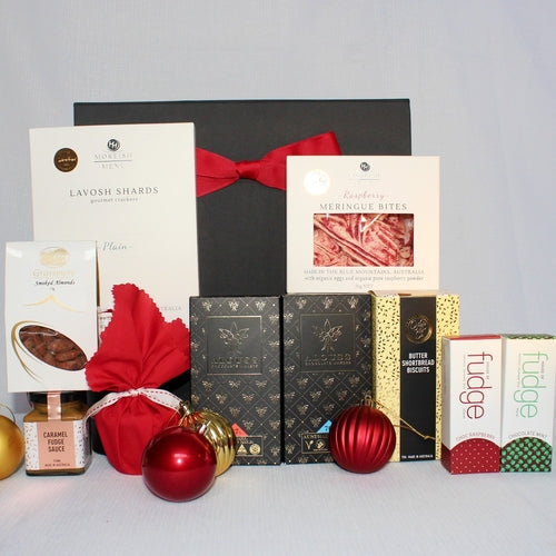 black gift box with red ribbon with a range of sweet and savoury foods in front - lavosh shards, smoked almonds, chocolate, fudge, raspberry meringue bites, shortbread and Christmas pudding with sauce - all Australian made