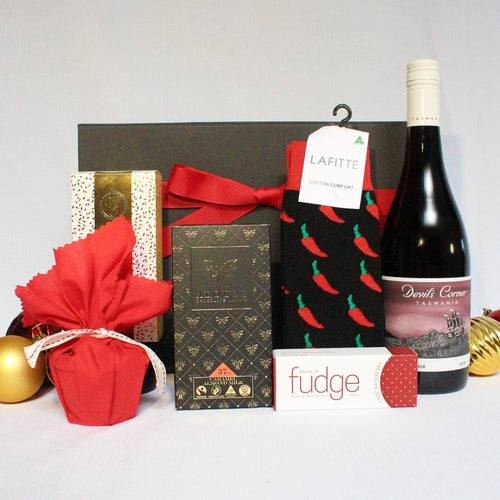 black gift box with red ribbon behind a bottle of Australian red wine, Australian made socks and sweet treats including chocolate and Christmas pudding