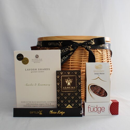 wicker picnic basket filld with snacks of nuts, handmade chocolate and fudge, lavosh shards and a cheese knife